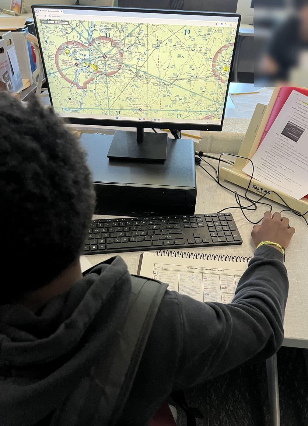 A student reads an FAA sectional chart on screen with the chart legend beside the keyboard
